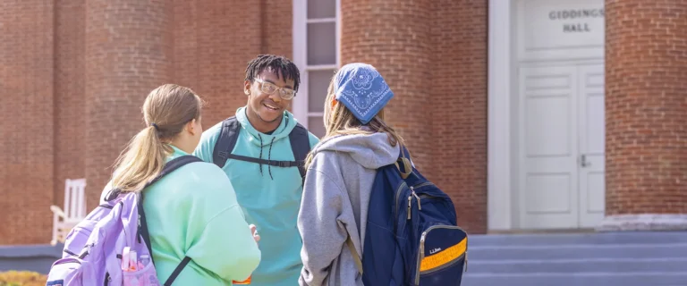 Three students talking in front of the doors of Giddings Hall.